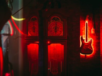 A large antique clock and an electric guitar outlined with red neon lights are displayed against a dark wall, creating a moody atmosphere.